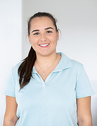 Eine MFA in einem hellblauen Poloshirt lächelt in die Kamera.