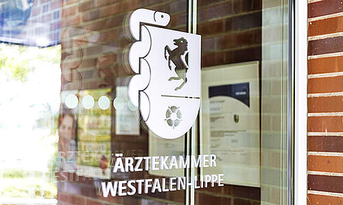 Foto der Eingangstür des Ärztehauses in Münster. Das Bild zeigt das weiße Kammerlogo auf der Glastür.